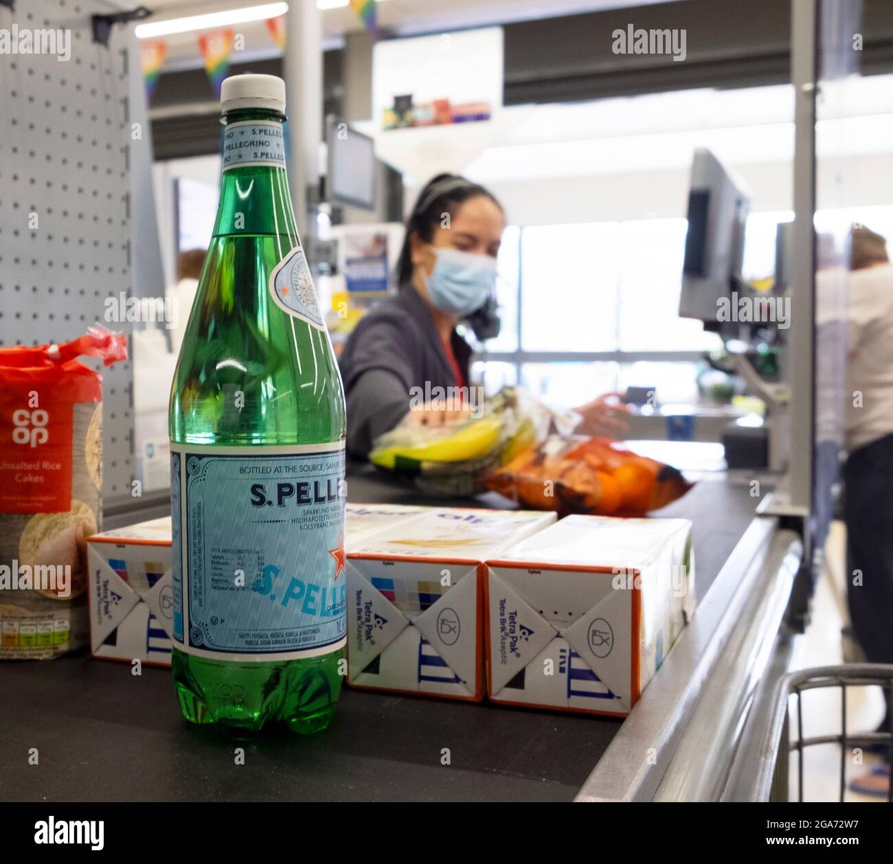 Junge Arbeiterin mit covid facemask im Co Op Supermarkt, die an der Kasse für Lebensmittel bei einer Pandemie arbeitete Großbritannien, Großbritannien, KATHY DEWITT Stockfoto