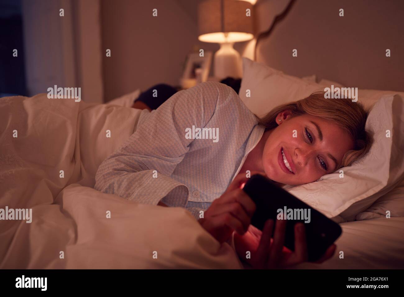 Ein Paar Mit Einer Frau, Die Nachts Im Bett Liegt Und Auf Den Bildschirm Des Mobiltelefons Schaut Stockfoto