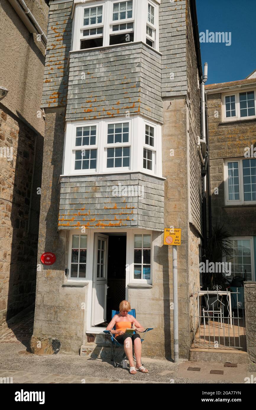 Frau, die vor einem Ferienobjekt am Hafen in St. Ives, Cornwall, Großbritannien, sitzt. Stockfoto