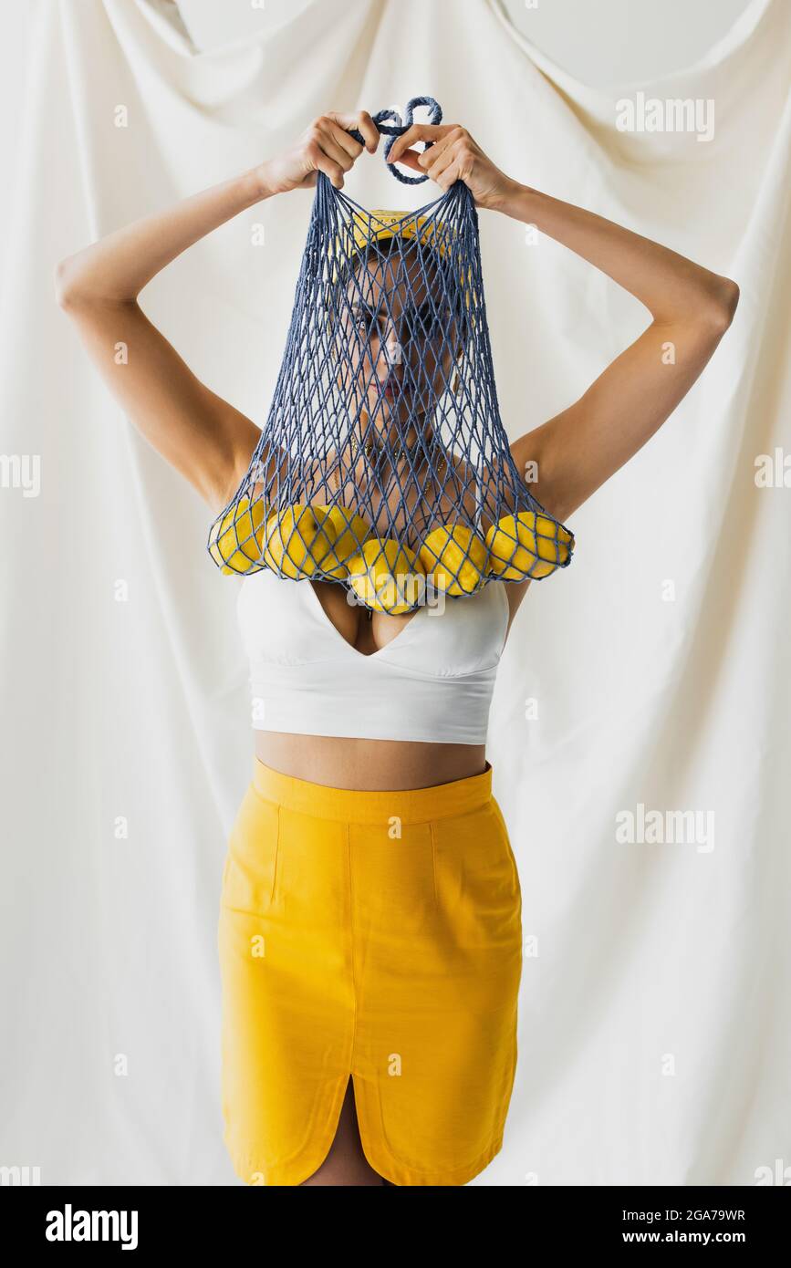 Frau in Crop Top hält Saitentasche mit Zitronen auf weiß Stockfoto