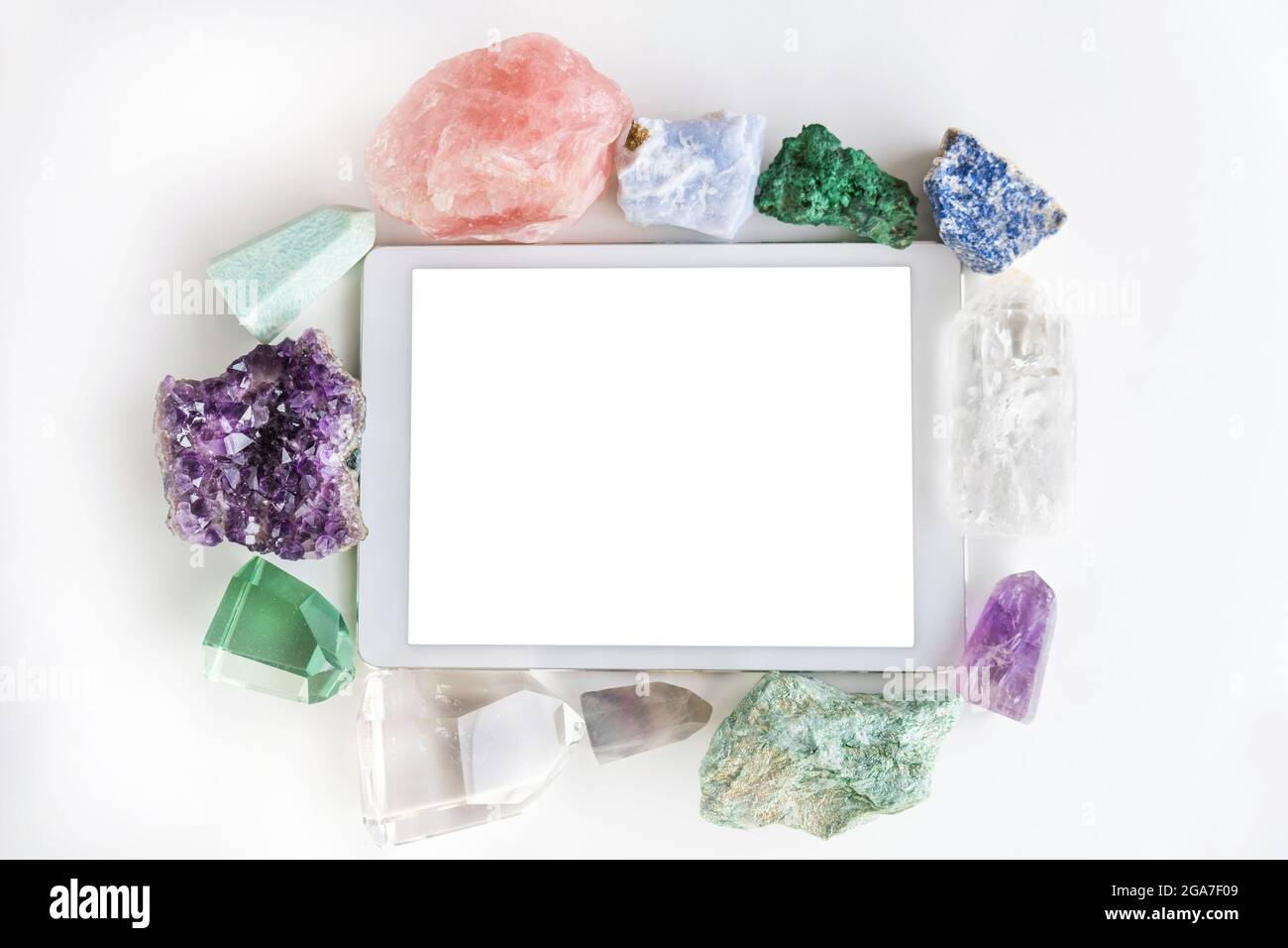 Weißes Touchpad mit leerem Touchscreen, eingerahmt von Kristallen und Edelsteinen auf weißem Hintergrund mit leerem Raum. Flacher Rahmen mit bunten Stockfoto