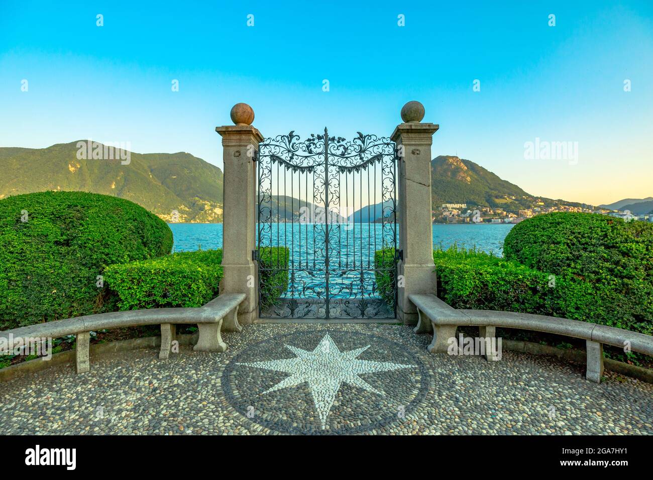 Tor am Luganer See im öffentlichen Ciani Park der Schweiz. Der Seeufer der Stadt Lugano im Kanton Tessin. Parkbank mit Windrose aus Steinen Stockfoto