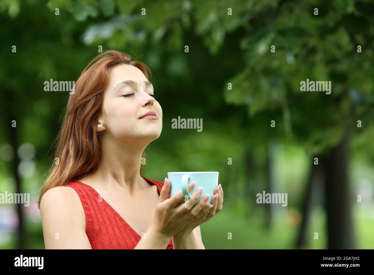 Eine entspannte Frau hält eine Tasse Kaffee und atmet frische Luft in einem Park Stockfoto