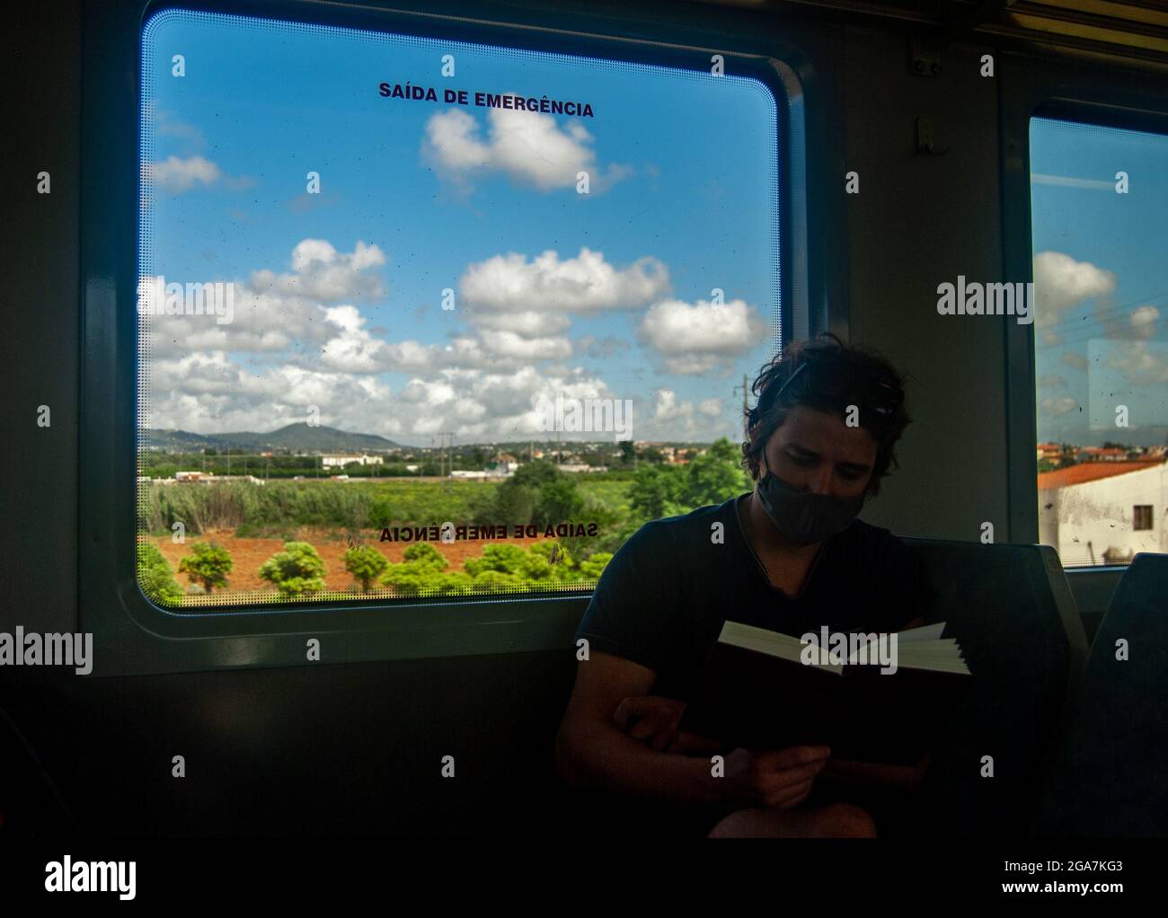 Ein Mann liest im Zug ein Buch, während sonnige portugiesische Landschaften im Fenster vorbeiziehen Stockfoto