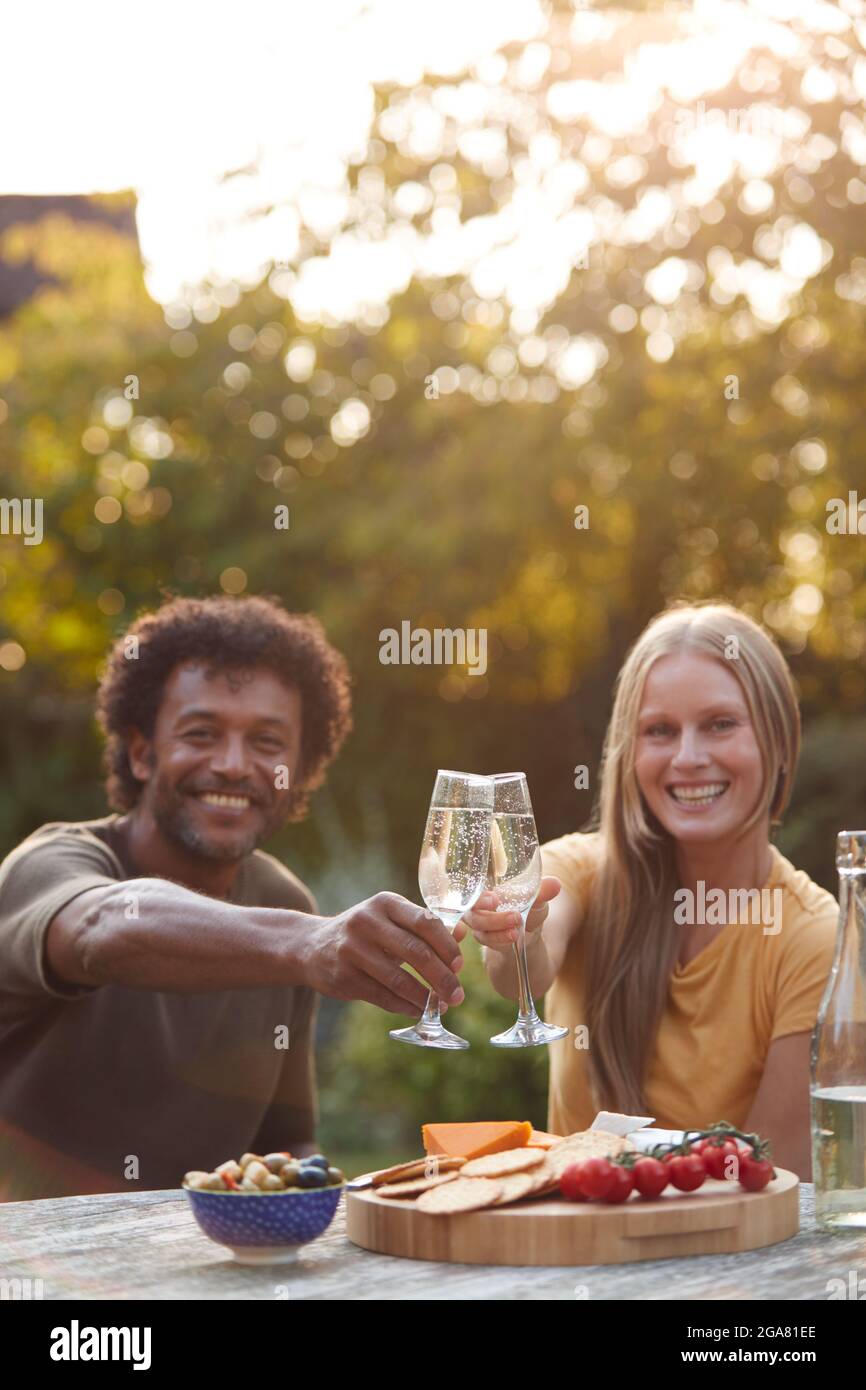 Portrait Eines Reifen Paares, Das Mit Champagner Feiert, Während Sie Mit Snacks Am Tisch Im Garten Sitzen Stockfoto