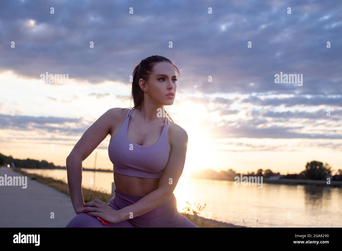 Junge kaukasische Frau in Sportkleidung, die bei Sonnenuntergang am Fluss posiert Stockfoto
