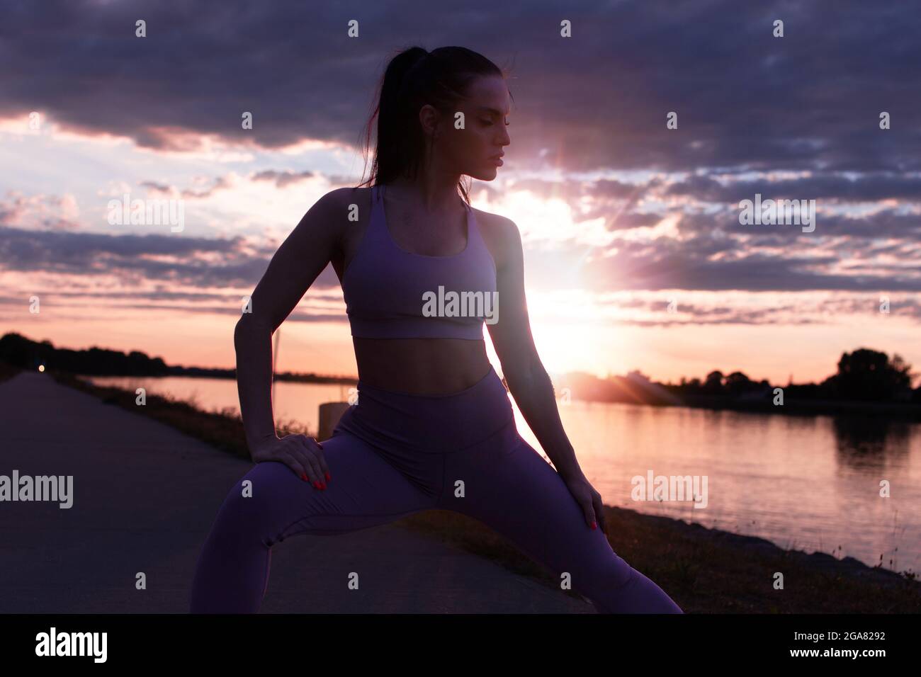 Junge Frau in Sportkleidung, die sich vor dem Laufen bei Sonnenaufgang dehnt, wärmt sich beim Training auf Stockfoto