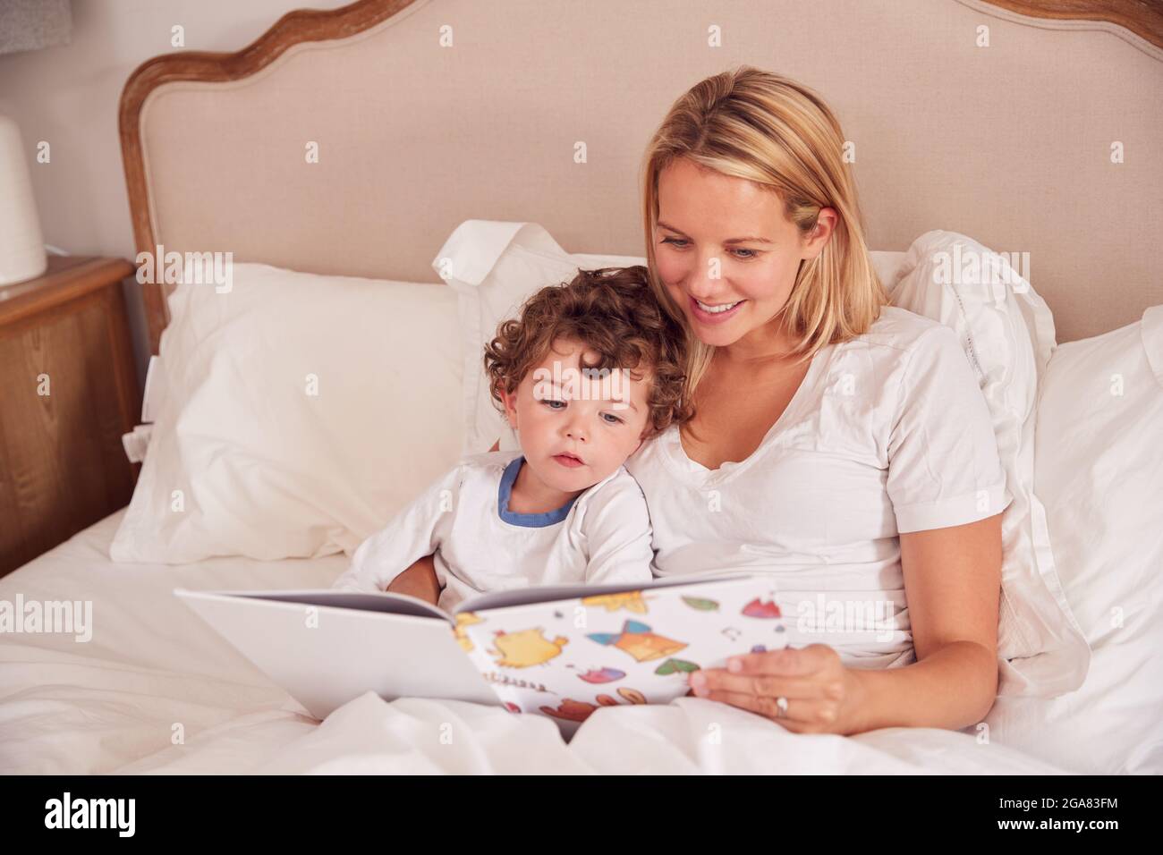 Mutter Im Schlafzimmer Beim Betrachen Des Bilderbuches Mit Jungem Sohn Im Schlafanzug Stockfoto