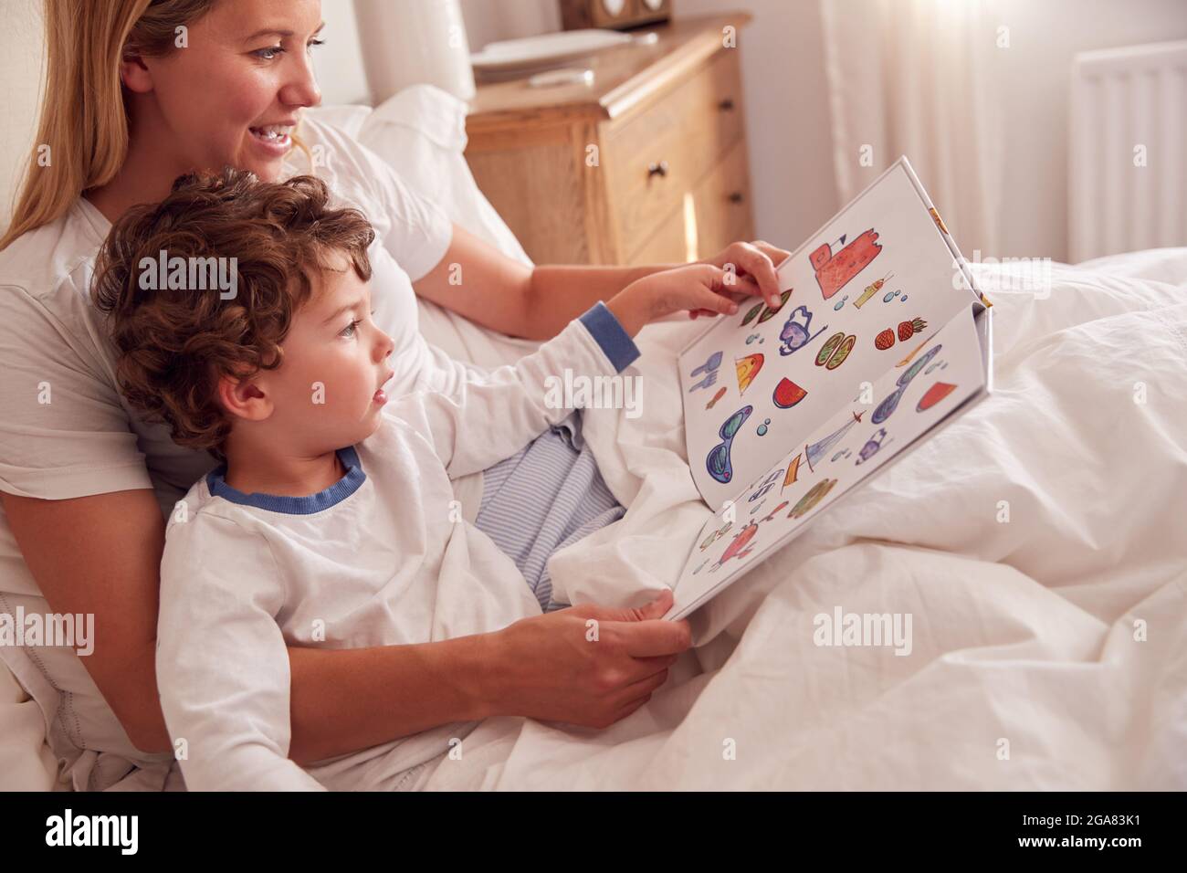 Mutter Im Schlafzimmer Beim Betrachen Des Bilderbuches Mit Jungem Sohn Im Schlafanzug Stockfoto