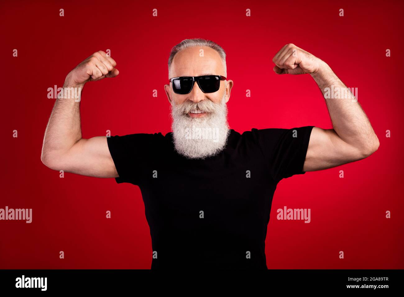 Porträt eines attraktiven älteren Rentners mit starkem, fröhlichen grauhaarigen Mann, der Muskeln zeigt, die auf einem hellroten Hintergrund isoliert sind Stockfoto