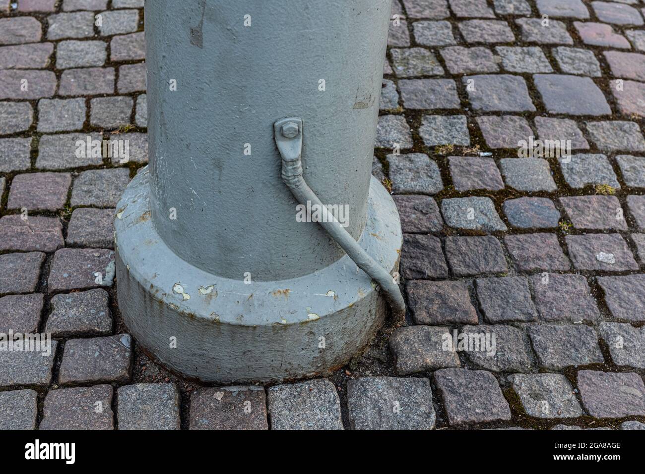 Elektrisches Erdkabel, das an einem Metallmast in einer gepflasterten Straße befestigt ist Stockfoto