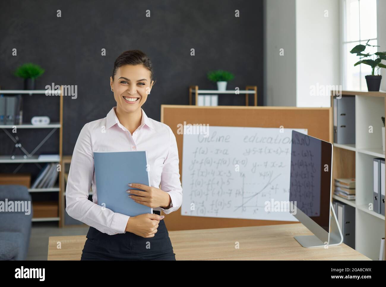 Porträt einer lächelnden jungen kaukasischen Lehrerin, die das Notenbuch in der Hand hält Stockfoto