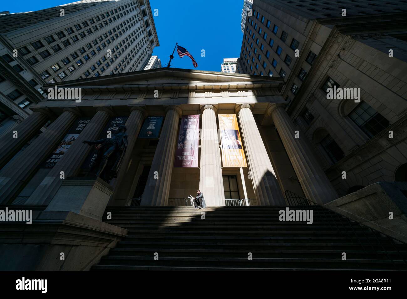 Ein Mann mit Gesichtsmaske und Hund sitzt auf der Treppe des Federal Hall Building NYC. Stockfoto