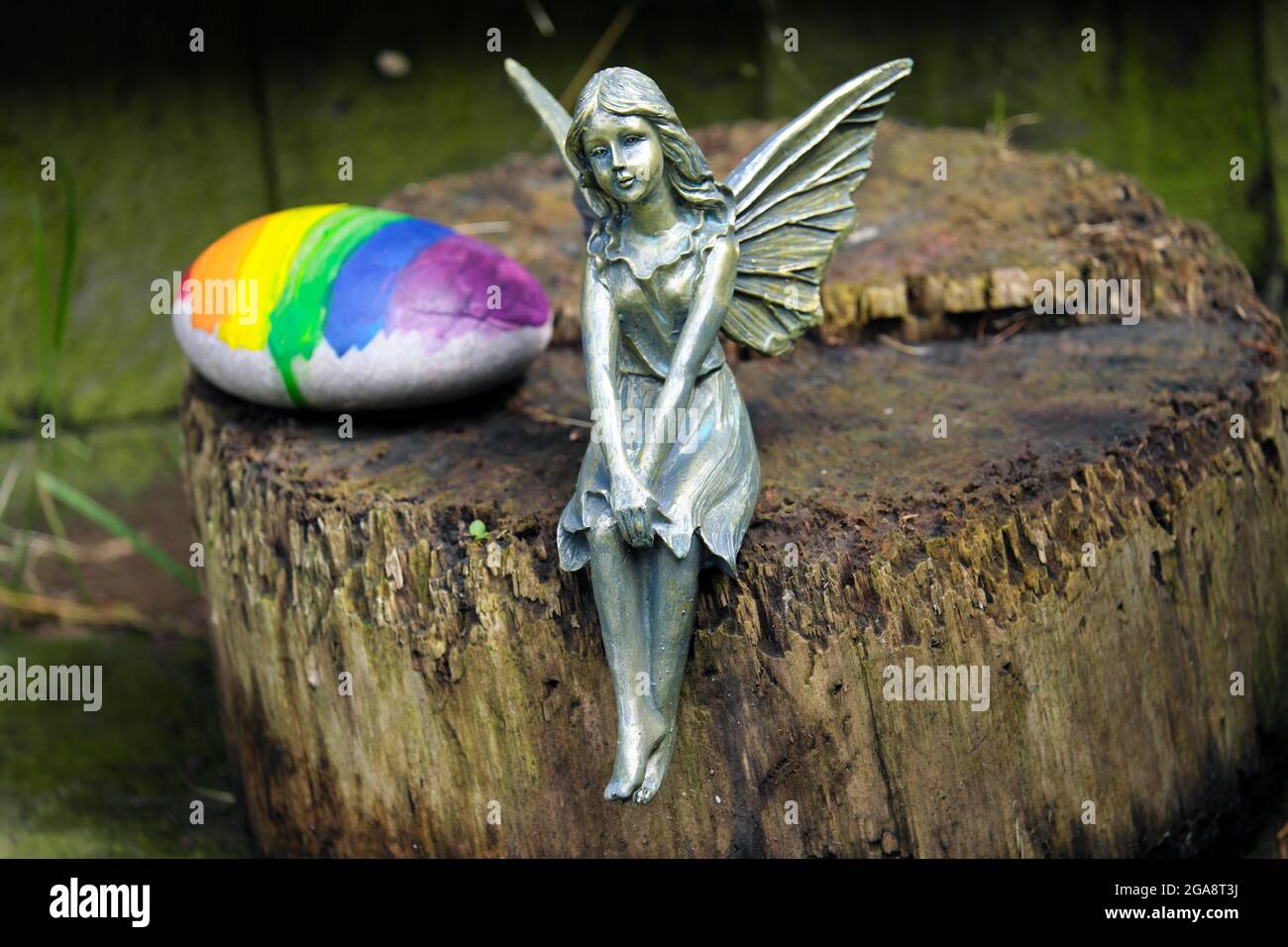 Eine Fee sitzt auf einem Baumstumpf mit einem regenbogenfarbenen Stein in einem englischen Landgarten England Stockfoto