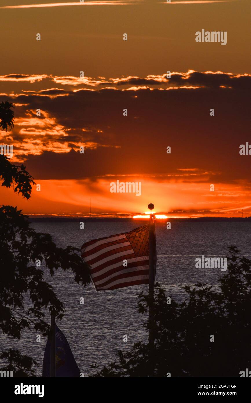 Die amerikanische Flagge flattert im Wind mit einem herrlichen Sonnenuntergang über Green Bay (Lake Michigan), der vom Park in Egg Harbor, Door County, Wisconsin, USA aus gesehen wird Stockfoto