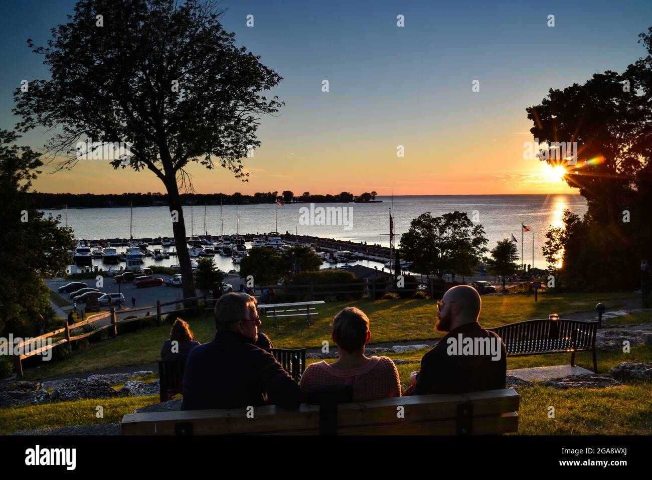 Menschen entspannen sich auf Bänken im Park, beobachten herrlichen Sonnenuntergang, Blick auf den Hafen mit Booten, in Egg Harbor, Door County, Wisconsin, USA Stockfoto