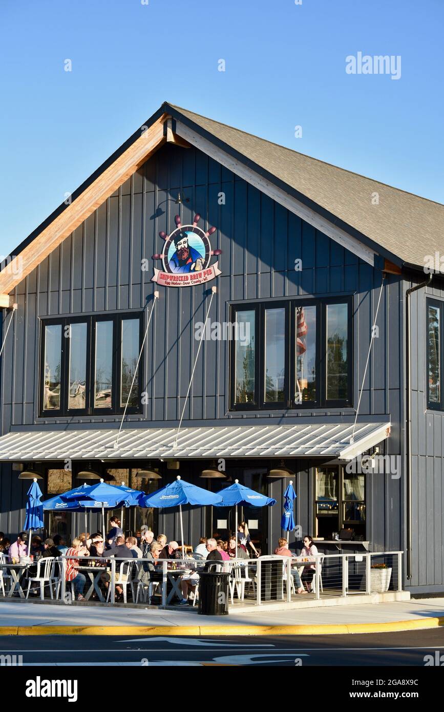 Menschen, die draußen essen und trinken, Speisen im Freien an Tischen mit Sonnenschirmen im Shipwrecked Brew Pub in Egg Harbor, Door County, Wisconsin, USA Stockfoto