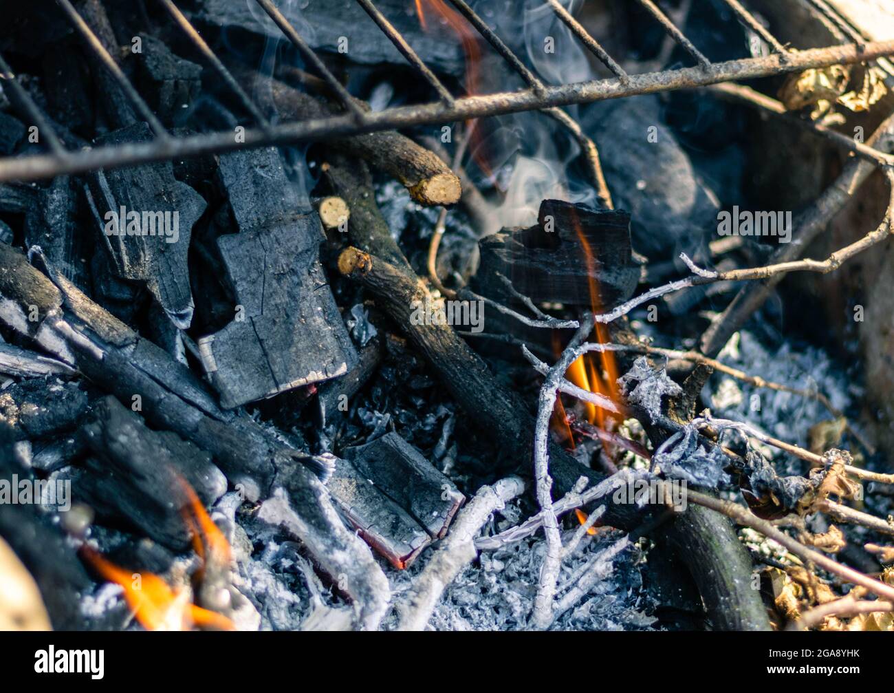 Holzkohle und Zweige, die unter dem Metallgitter brennen Stockfoto