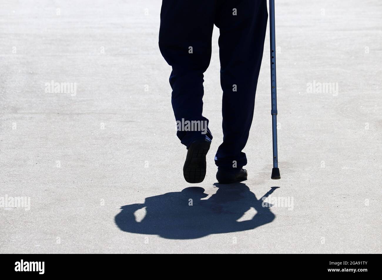 Silhouette eines Mannes, der mit einem Stock die Straße hinunter läuft, Schatten auf Asphalt. Konzept des Alters, Erkrankungen der Wirbelsäule oder Gelenkerkrankungen, ältere Menschen Stockfoto