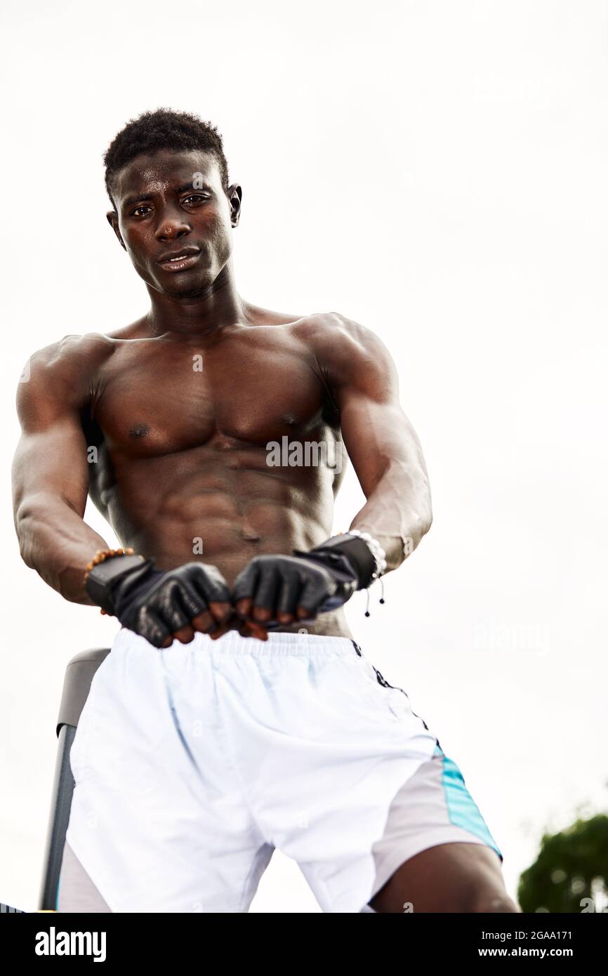 Muskulöser schwarzer Profi-Boxer schwitzt in Handschuhen beim Boxtraining im Freien, junger afroamerikanischer Boxer beim Training auf dem Straßenspielplatz. Stockfoto