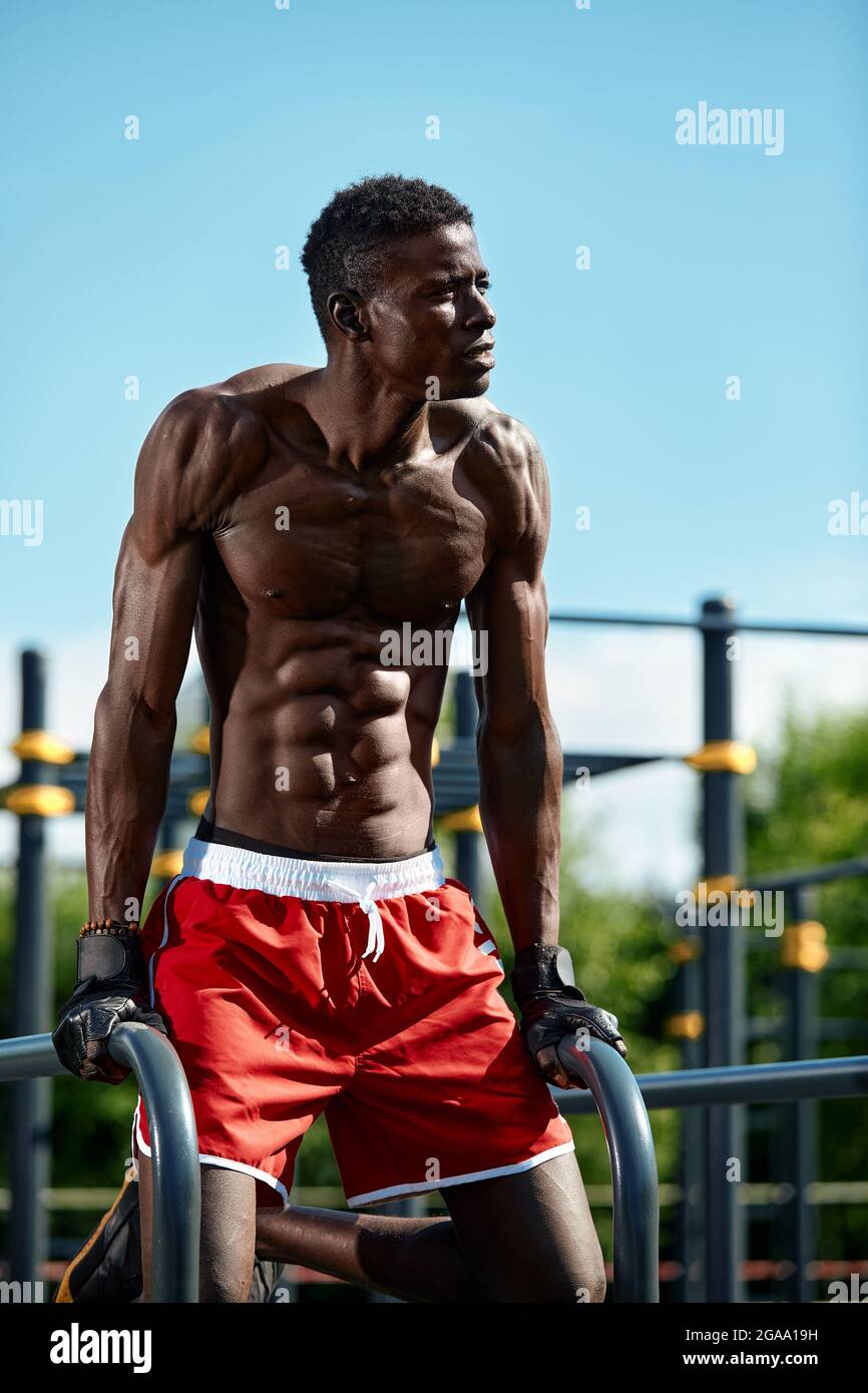 Schwarzer junger Mann, der auf den unebenen Bars im Park trainiert, Crossfit-Konzept, afroamerikanischer Mann, der Übungen auf den unebenen Bars auf der Straße macht, weiter Stockfoto