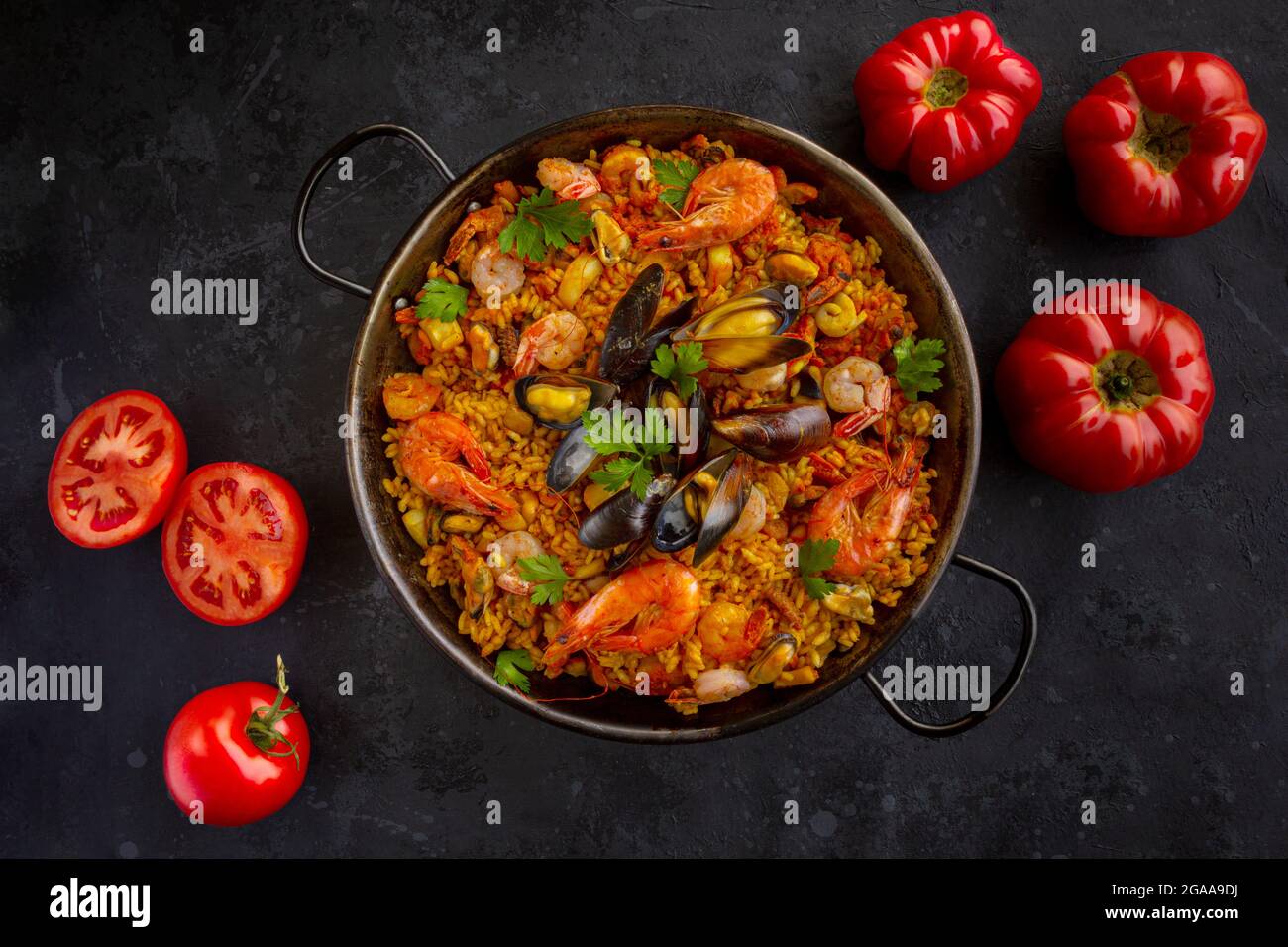 Traditionelle spanische Paella mit Meeresfrüchten und Tomaten auf schwarzem Hintergrund Stockfoto