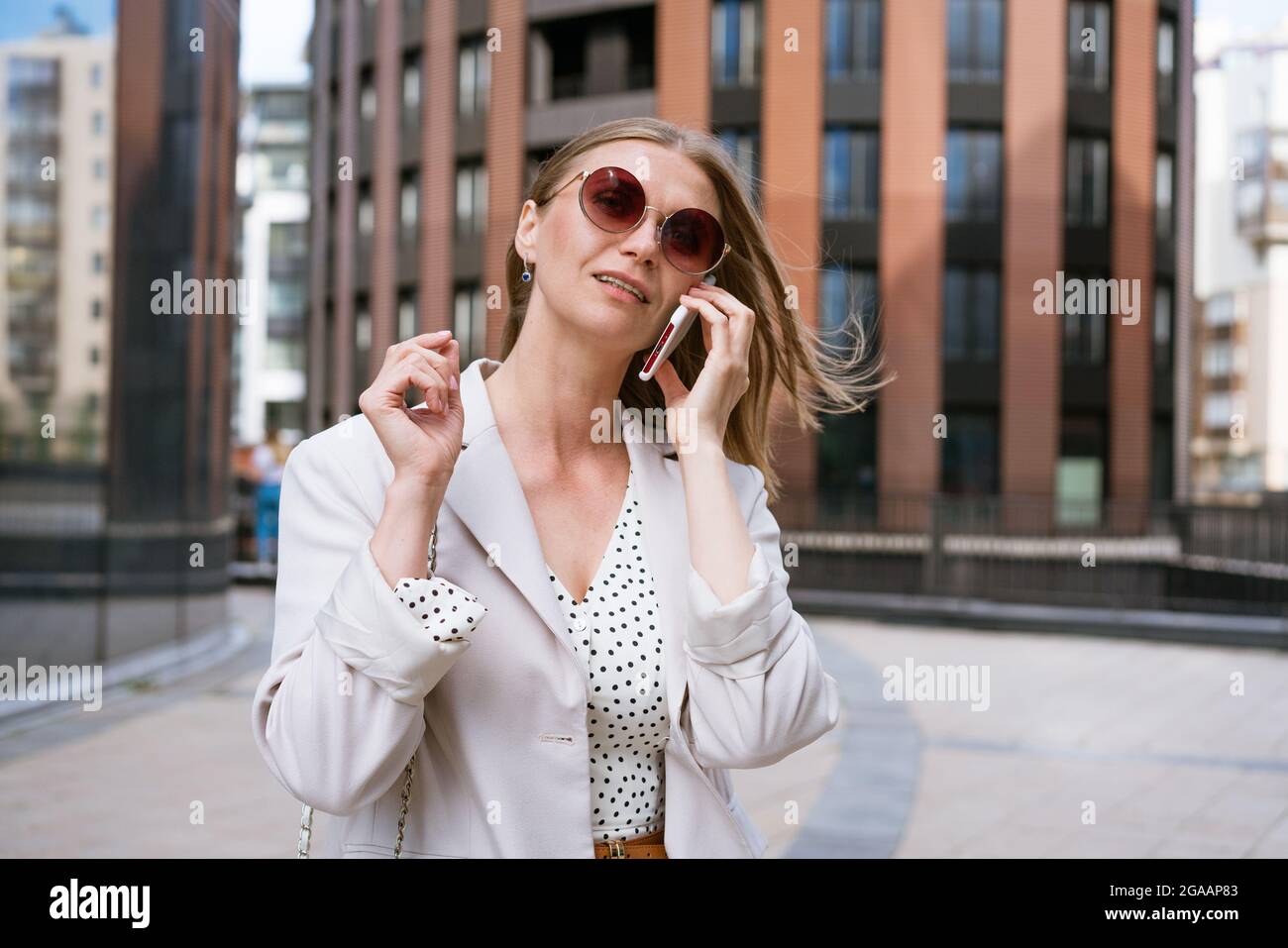 Geschäftsfrau mit Telefon in der Nähe des Büros. Portrait von schönen lächelnden Mädchen in modischen leichten Bürokleidung, Telefonieren, im Freien stehend in Sonnenbrille. Telefonkommunikation. Stockfoto