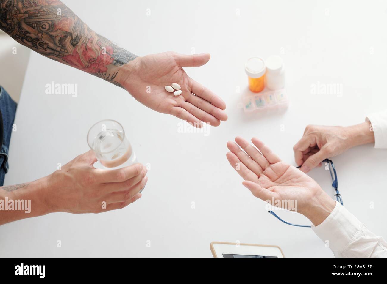 Nahaufnahme eines Mannes, der seiner Mutter Pillen und ein Glas Wasser gab, während sie am Tisch saß Stockfoto