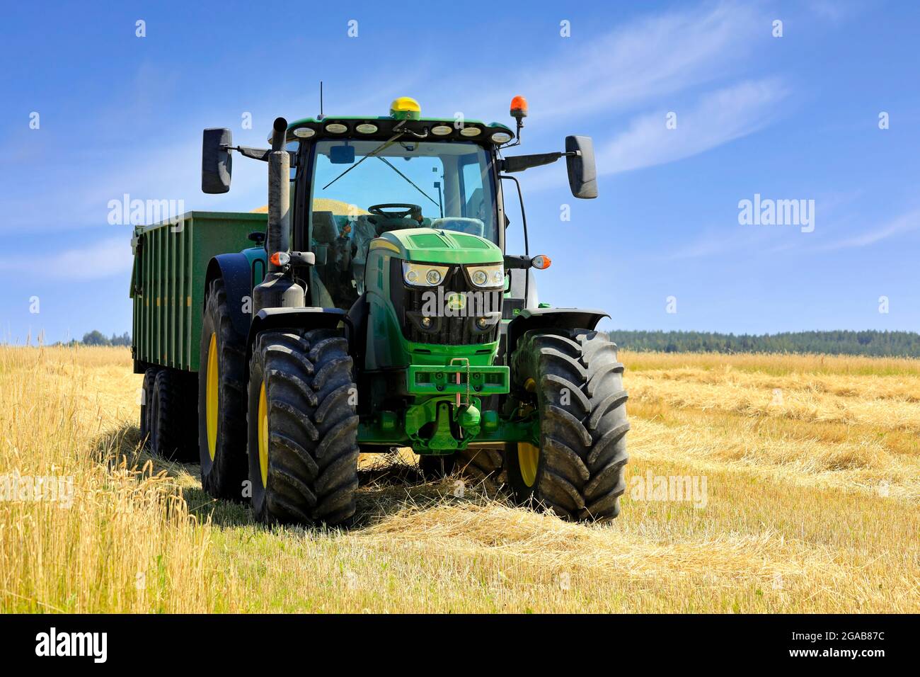 John Deere 6155R Traktor und Kire Anhänger voller geerntetem Weizen auf dem Feld an einem schönen Tag. Salo, Finnland. 25. Juli 2021. Stockfoto