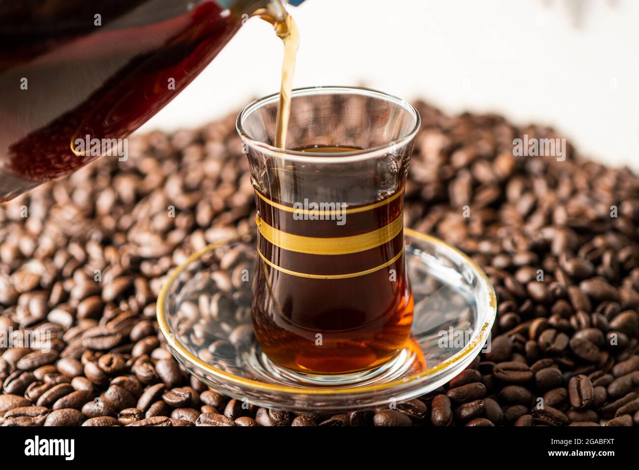 Mann hält und gießt Kaffee in eine Glastasse auf gerösteten Kaffeebohnen Stockfoto