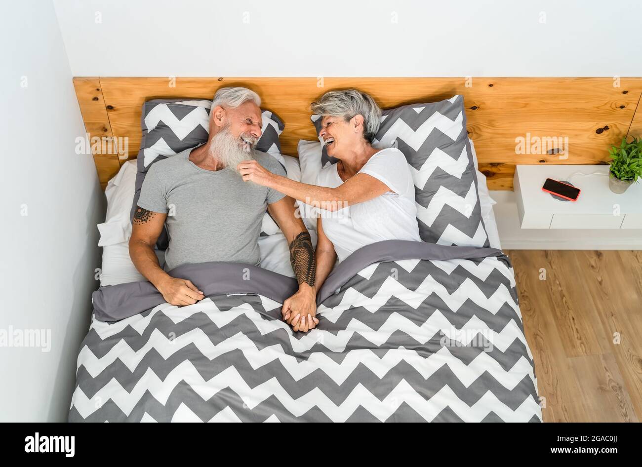 Glückliches Senioren-Paar, das zusammen lacht, während es im Bett unter Decken liegt - älterer Lebensstil und Liebesbeziehung Konzept Stockfoto