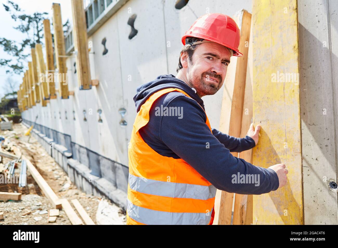 Bauarbeiter als Tischler mit rotem Hut auf der neuen Baustelle mit Holzbrett Stockfoto