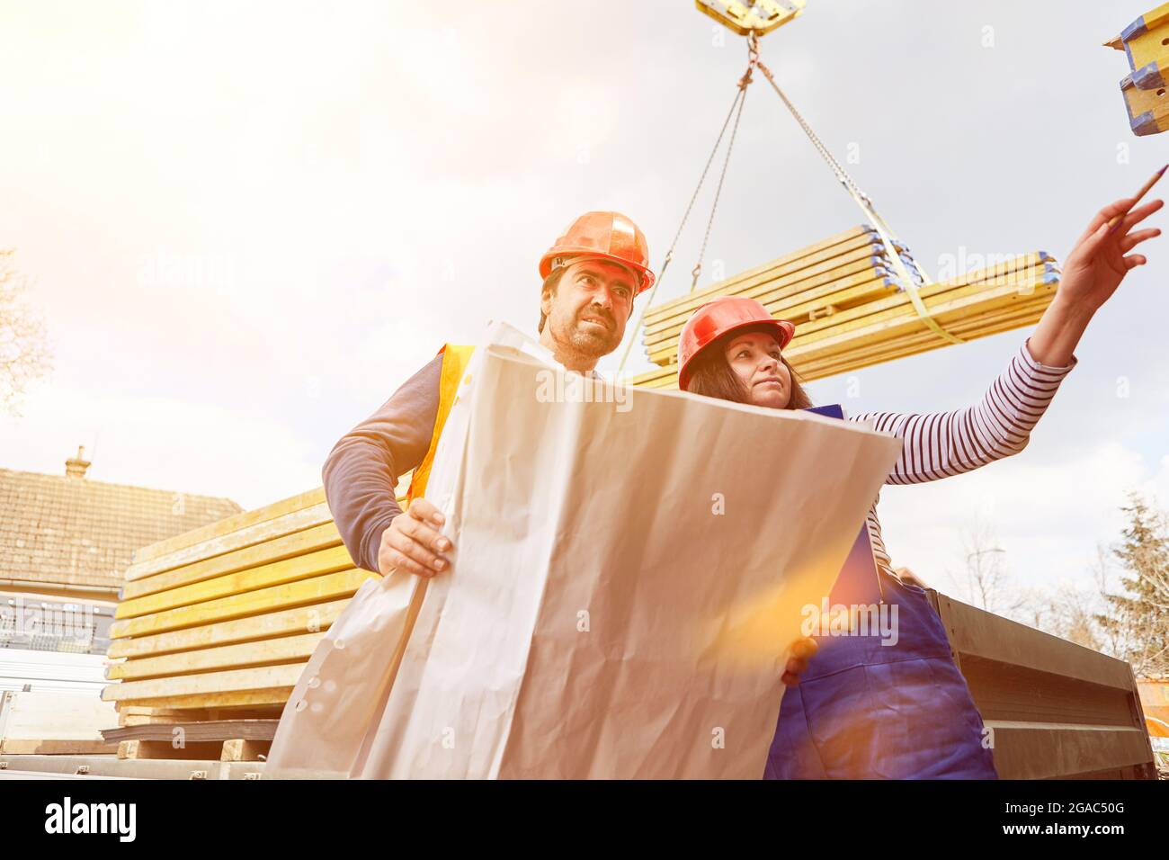 Lieferung von Holz und Baustoffen auf die Baustelle mit zwei Bauarbeitern und einem Bauplan Stockfoto