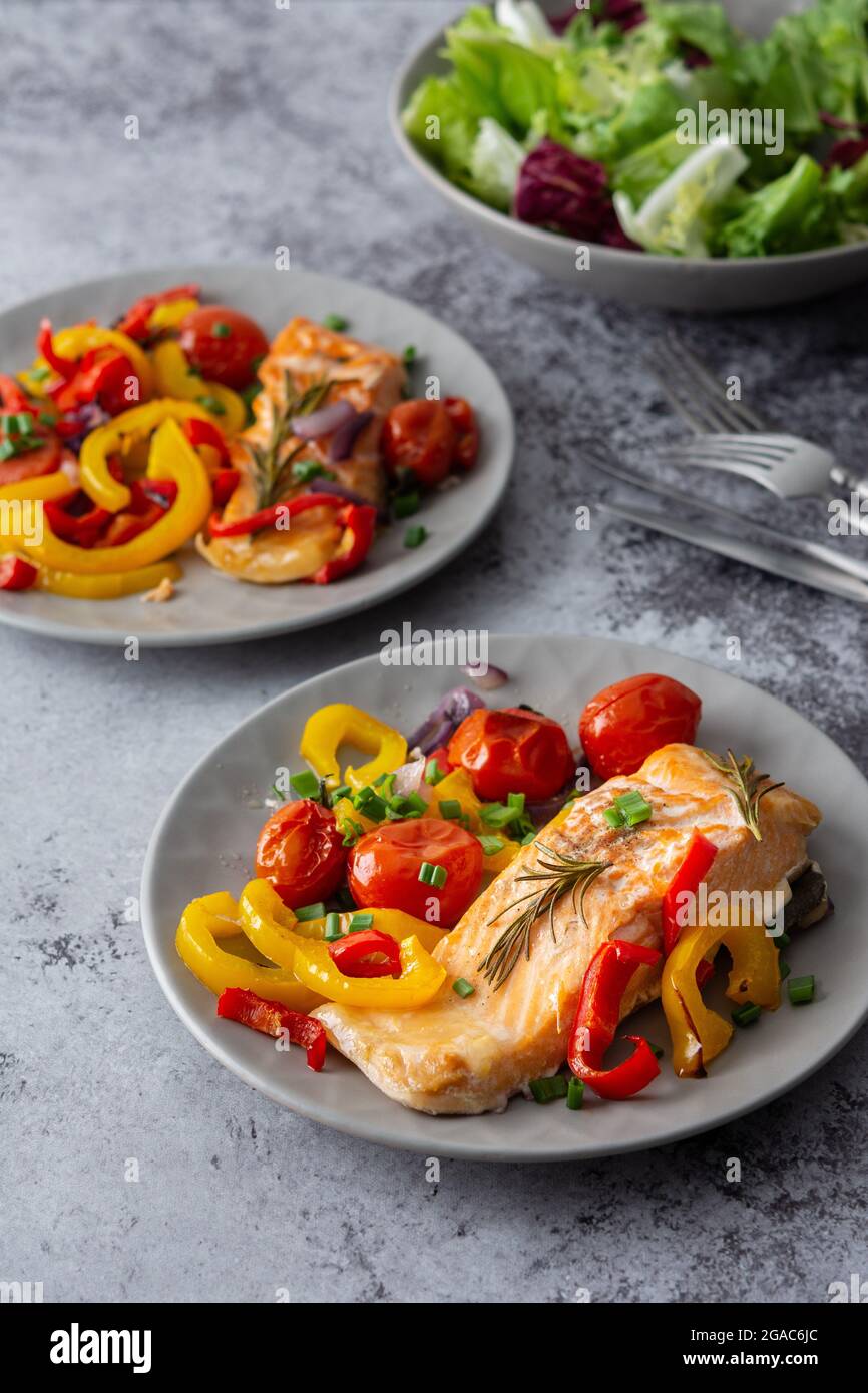 Gebackenes rotes Fischfilet Arctic Saibling auf einem Teller mit Gemüse, Salat in einer Schüssel mischen, leckeres herzhaftes gesundes Abendessen Stockfoto