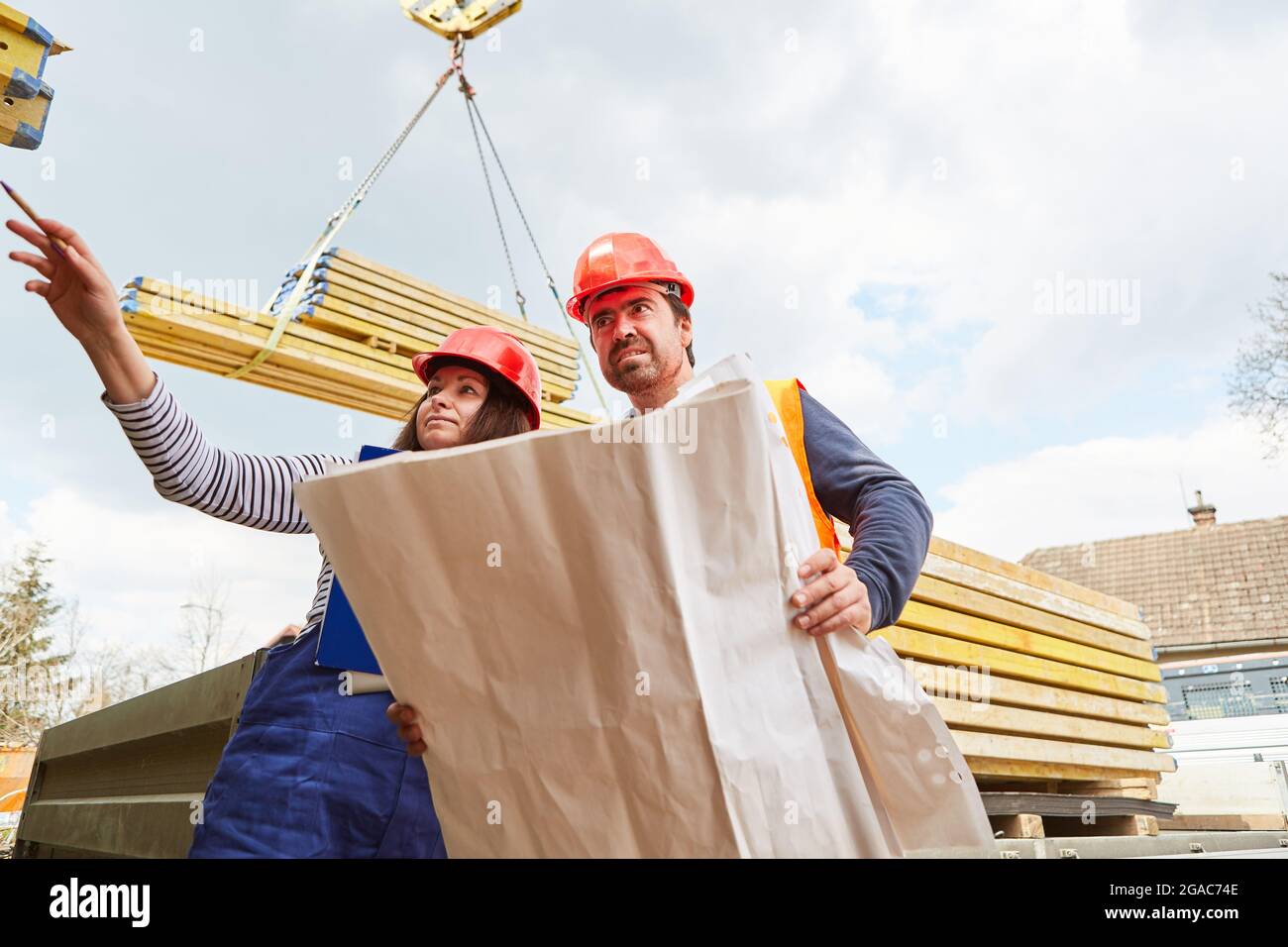 Architekt und Handwerker mit Blaupause auf der Baustelle mit Baustoffen auf dem Kran im Hintergrund Stockfoto
