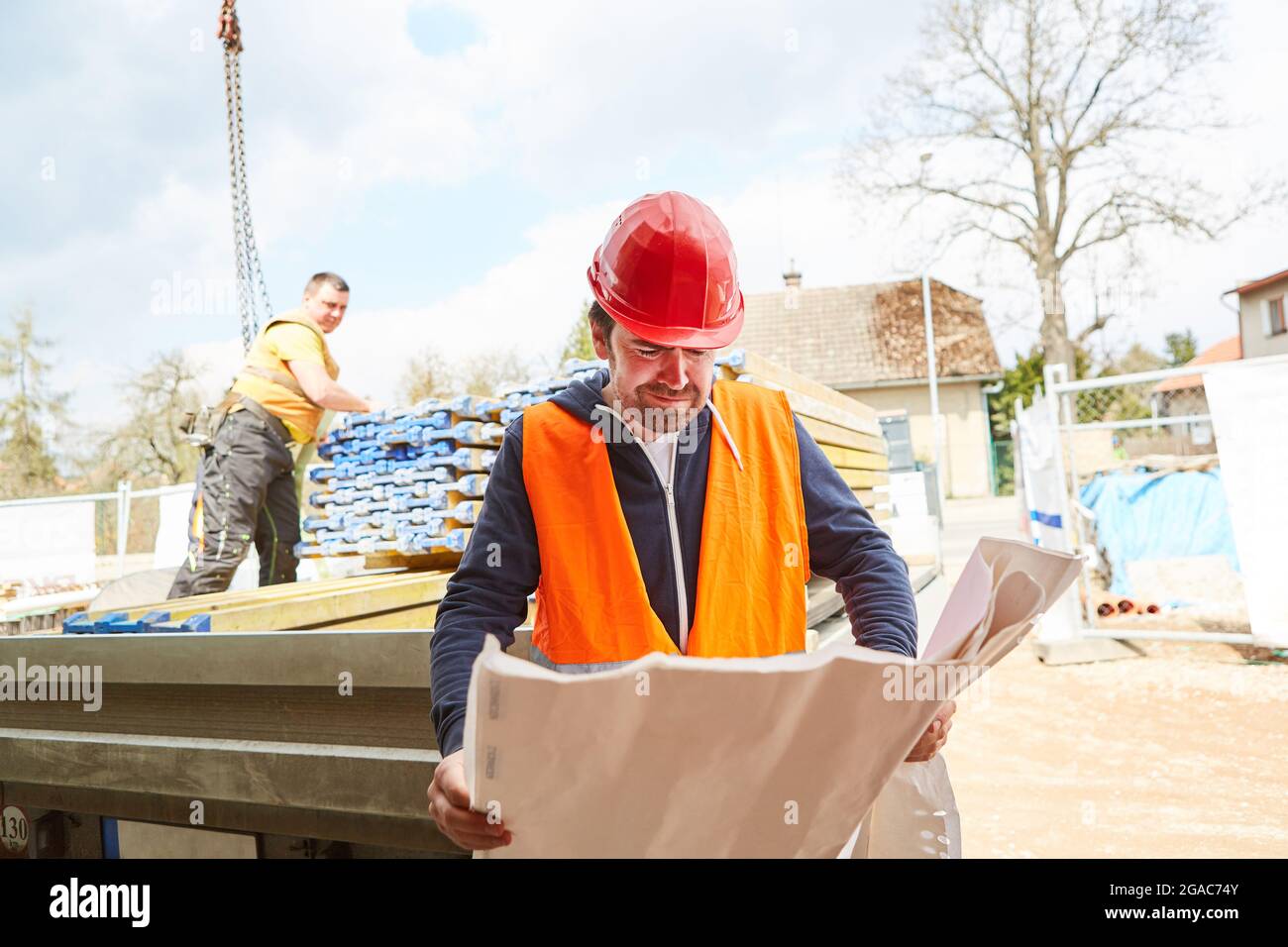 Vorarbeiter mit Architekturzeichnung auf der Baustelle mit Baumaterialien auf einer Ladefläche im Hintergrund Stockfoto