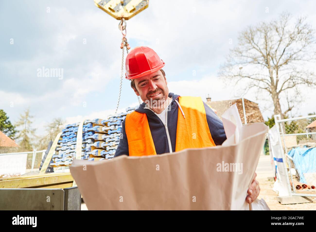 Architekt oder Vorarbeiter mit Bauplan auf der Baustelle mit Lieferung von Holz im Hintergrund Stockfoto