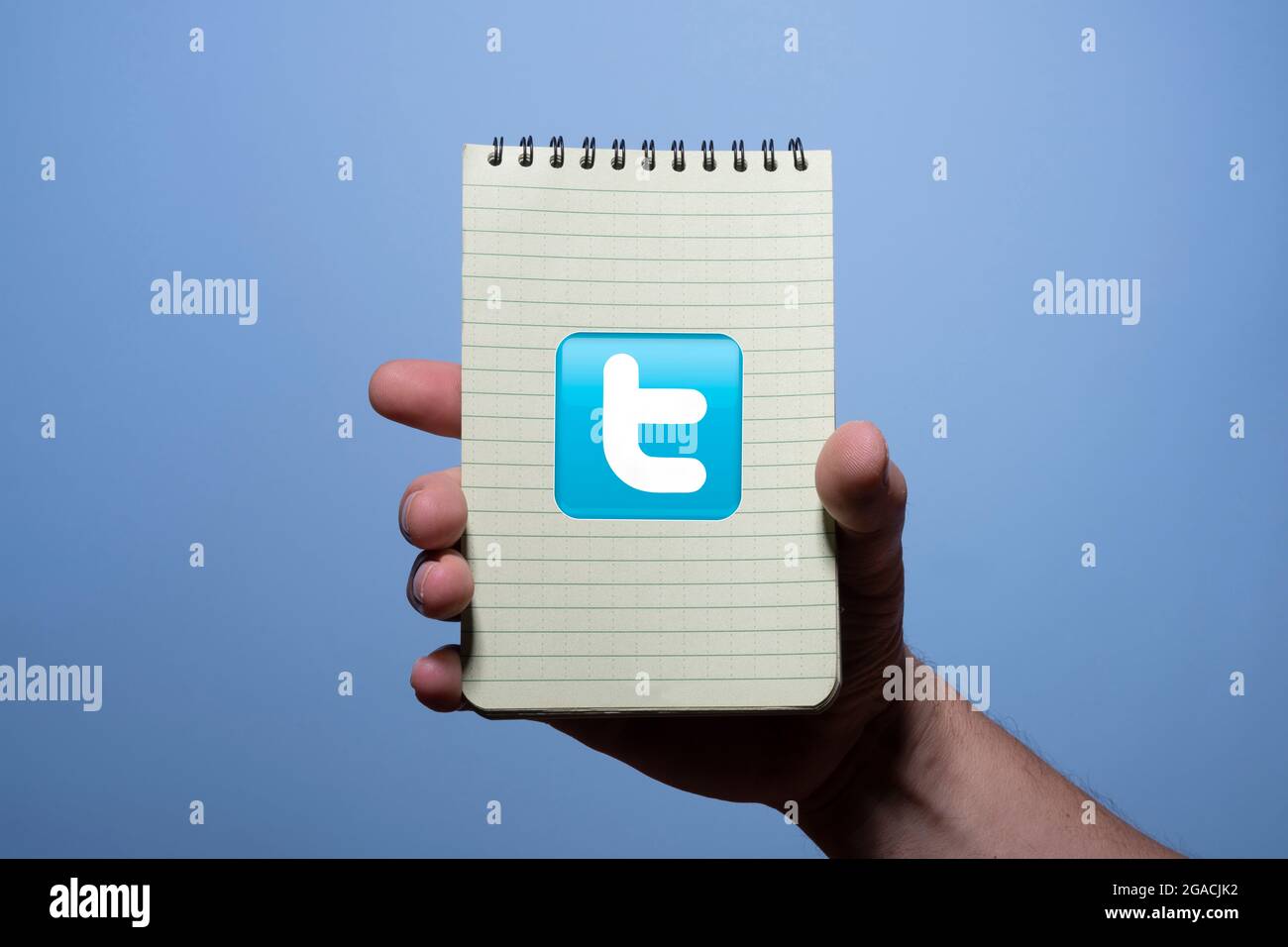 Ein Notizblock mit dem Twitter-Symbol in der Hand eines Mannes mit blauem Hintergrund Stockfoto