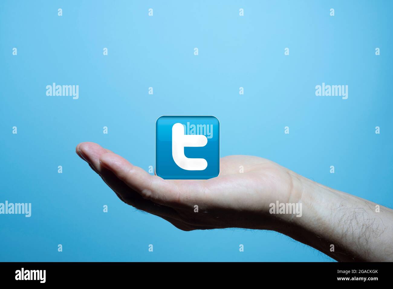 Twitter-Symbol in der Handfläche eines Mannes mit blauem Hintergrund Stockfoto