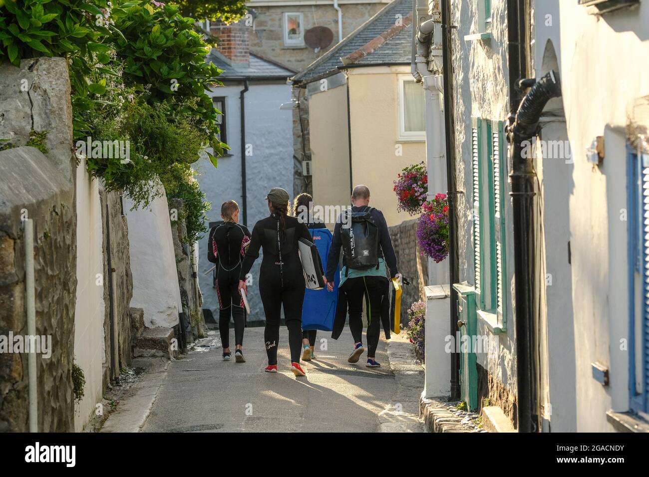 Familie in Neoprenanzügen auf dem Weg zum Strand in einer engen Straße in St. Ives, Cornwall, Großbritannien. Stockfoto