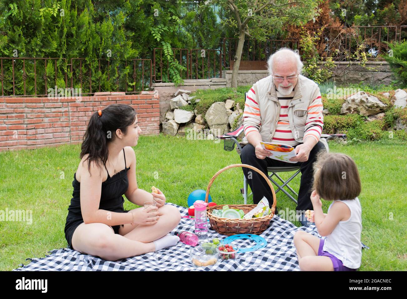 Die Mädchen picknicken mit ihren Großeltern. Der alte Mann sitzt auf dem Stuhl. Stockfoto