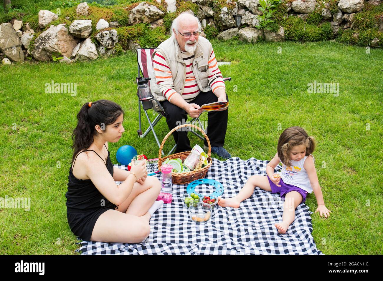 Die Mädchen picknicken mit ihren Großeltern. Der alte Mann sitzt auf dem Stuhl. Stockfoto