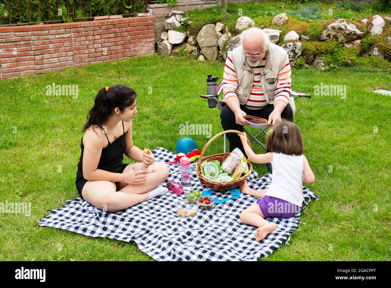 Die Mädchen picknicken mit ihren Großeltern. Der alte Mann sitzt auf dem Stuhl. Stockfoto