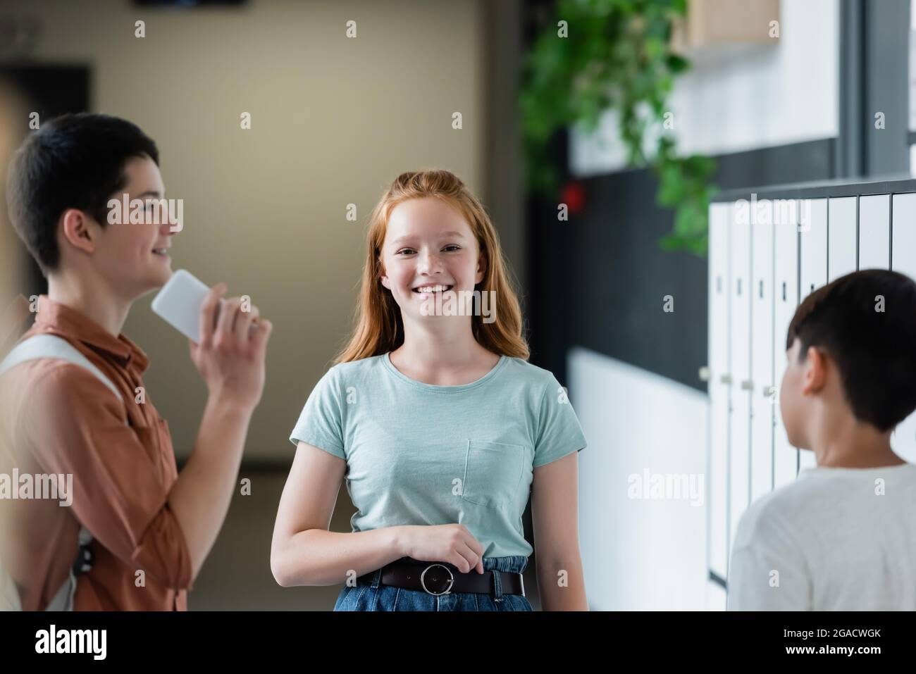 Rotschopf-Mädchen lächelt vor der Kamera in der Nähe von Teenagern in der Schulhalle Stockfoto