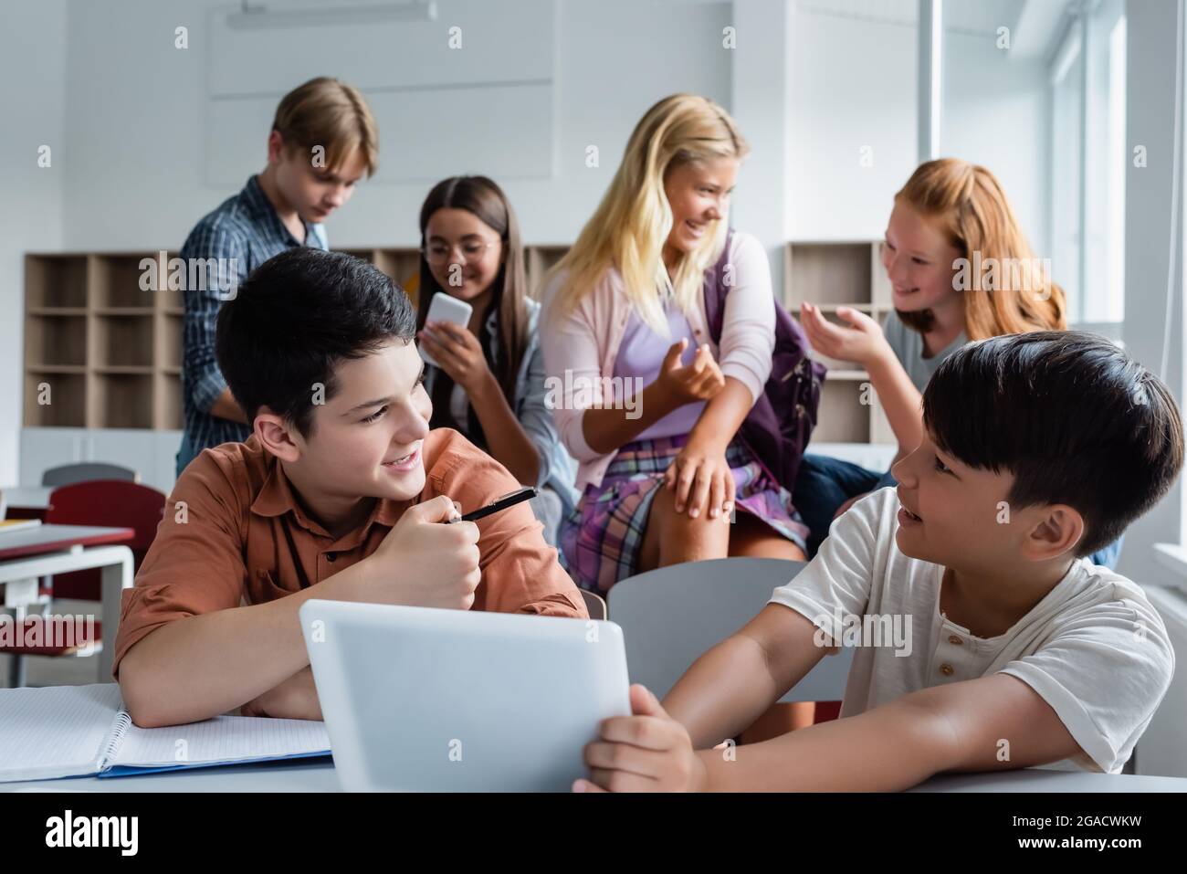 Fröhliche asiatische Kind hält digitale Tablette in der Nähe von Freund und Klassenkameraden Stockfoto