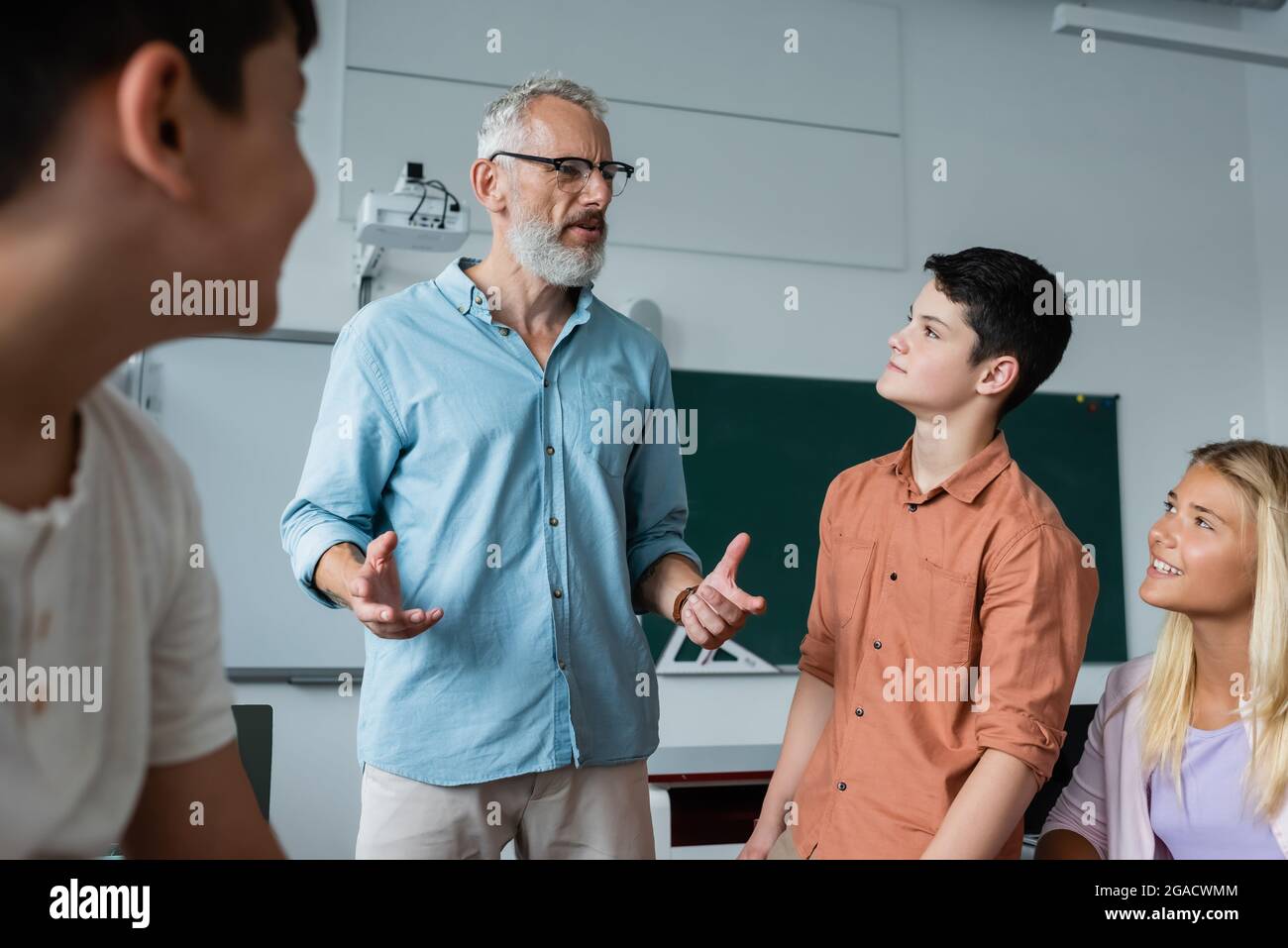 Grauhaarige Lehrerin gestikulierte, während sie im Klassenzimmer mit Teenagern sprach Stockfoto