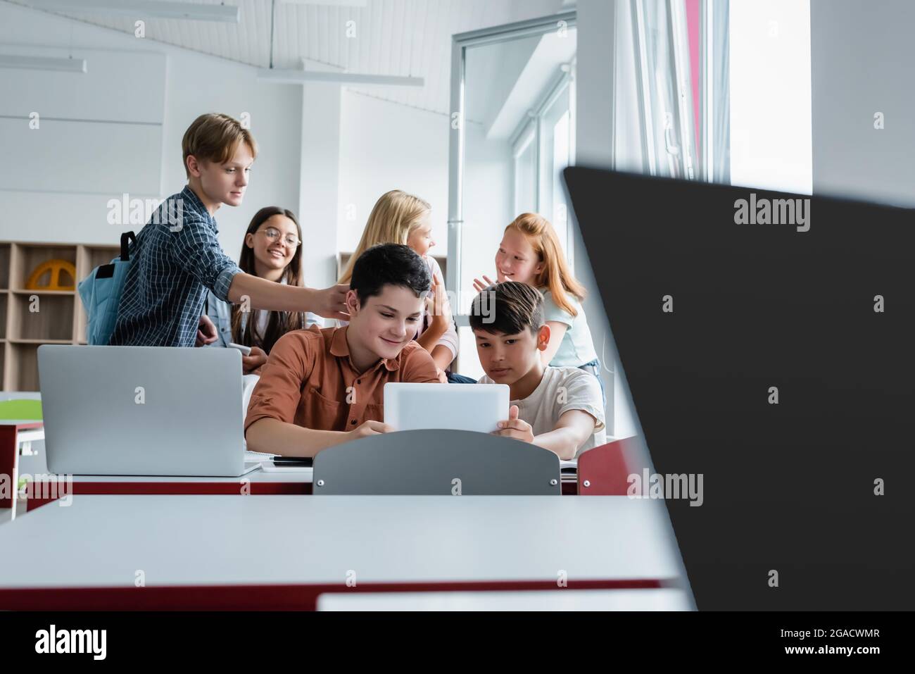 Interracial Schüler mit digitalen Tablet in der Nähe von Laptops und Freunden Stockfoto