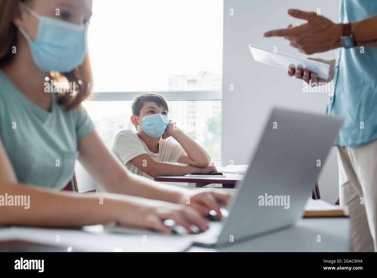 Asiatische Schüler in medizinische Maske Blick auf verschwommene Lehrer mit digitalen Tablet Stockfoto