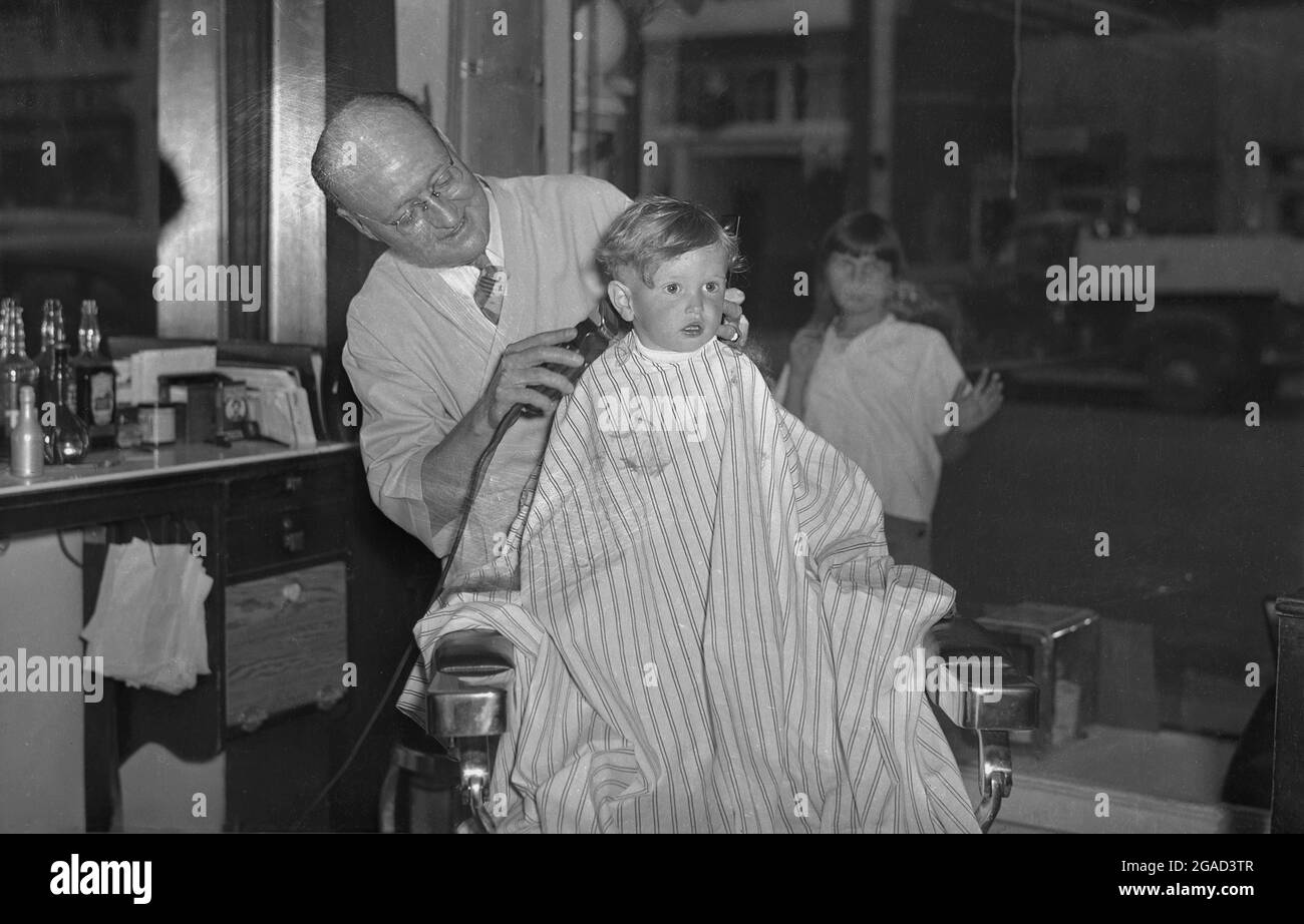 1940s, historisch, ein kleiner Junge, der in einem traditionellen Friseurstuhl mit einem gestreiften Gewand sitzt, um einen Haarschnitt zu bekommen, USA. Stockfoto