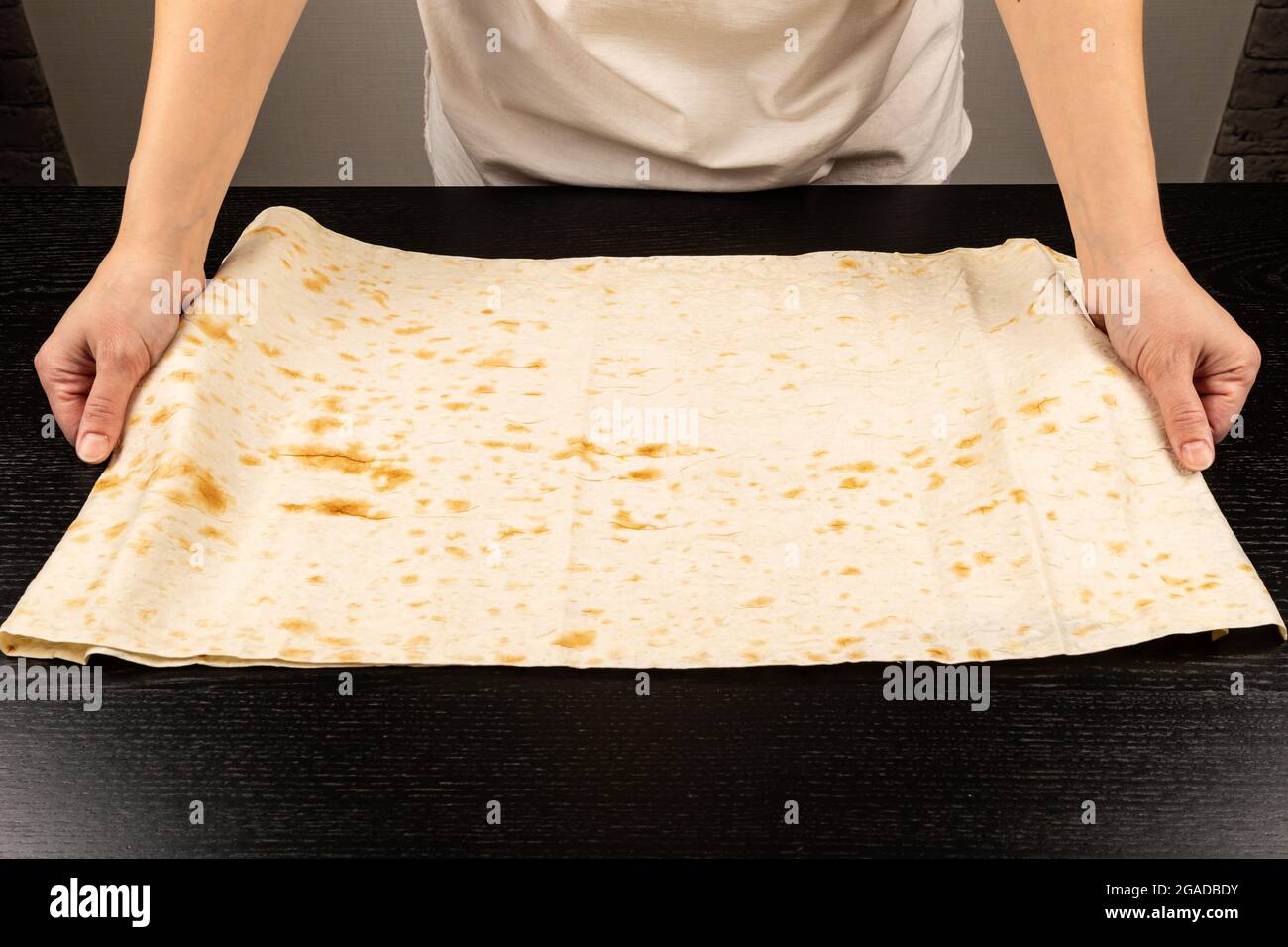 Weibliche Hände legen frisches Pita-Brot für die Herstellung von Shawarma Auf dem Hintergrund eines schwarzen Holztisches Nahaufnahme Stockfoto